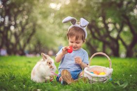 small child sitting on the grass wearing bunny ears with bunny and egg filled easter basket