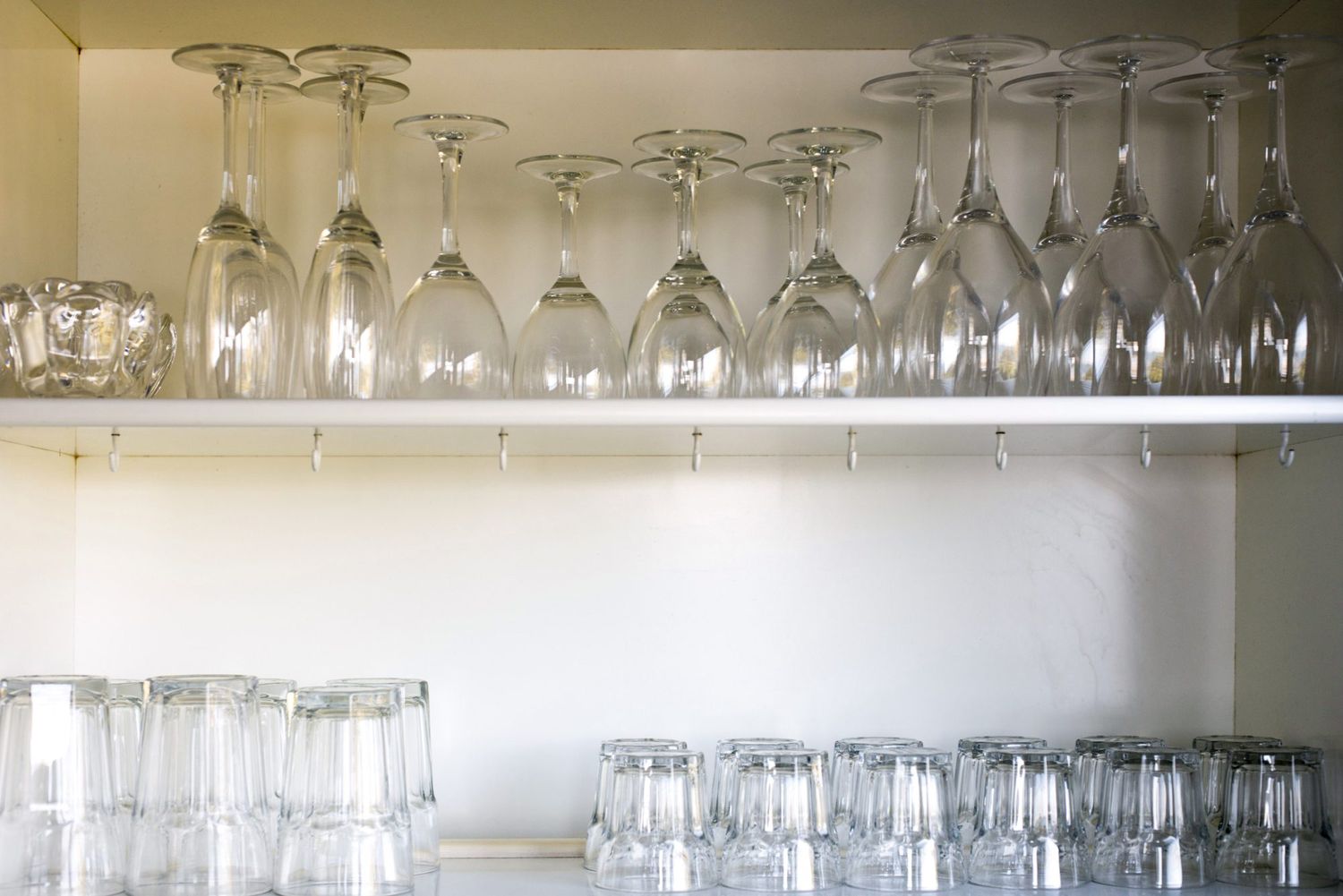 Clean glassware neatly arranged on open white wooden shelves