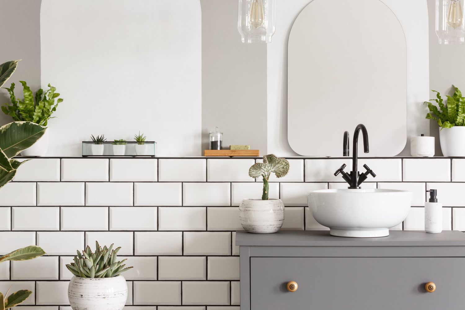 photo of a sink on a cupbaord in a bathroom interior with tiles, mirror and plants