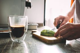 cutting avocado on a wooden cutting board for toasts. Glass mug with hot coffee