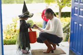 Little girl dressed as witch for halloween trick-or-treating on doorstep for candy