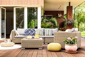 Beige garden furniture with striped pillows on wooden terrace with pink flowers and poufs