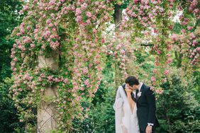 bride and groom kissing beneath trellis of pink flowers