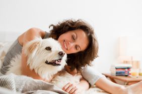 Smiling woman petting dog in bed